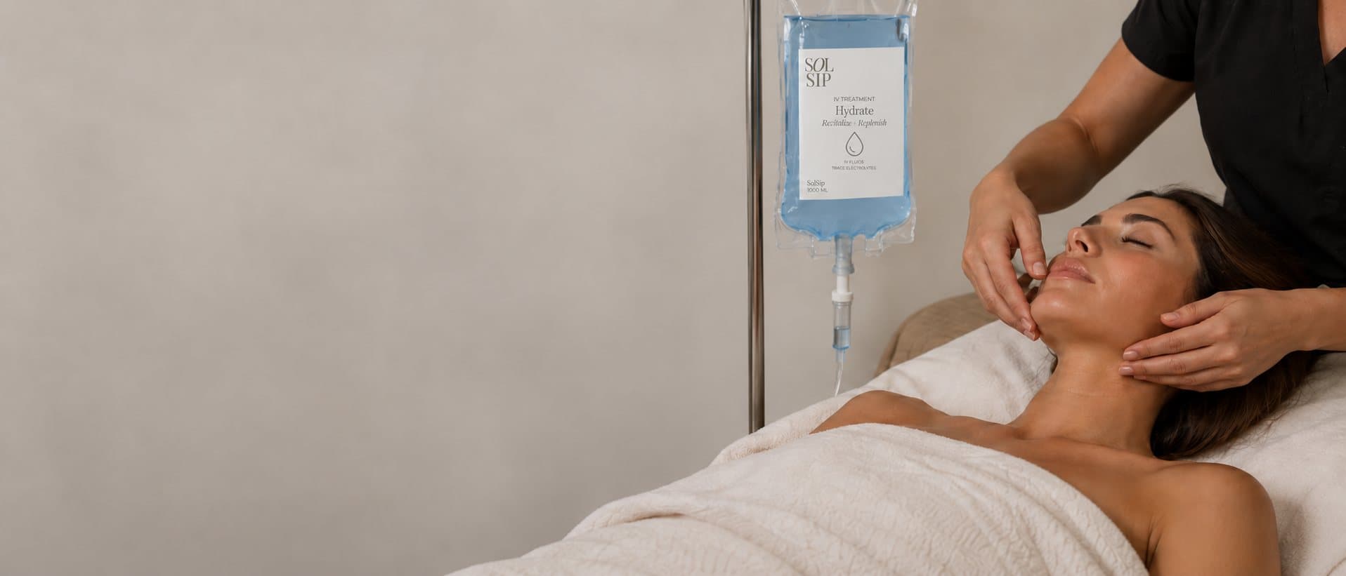 A SolSip client resting during a facial, with a SolSip IV bag hanging beside her