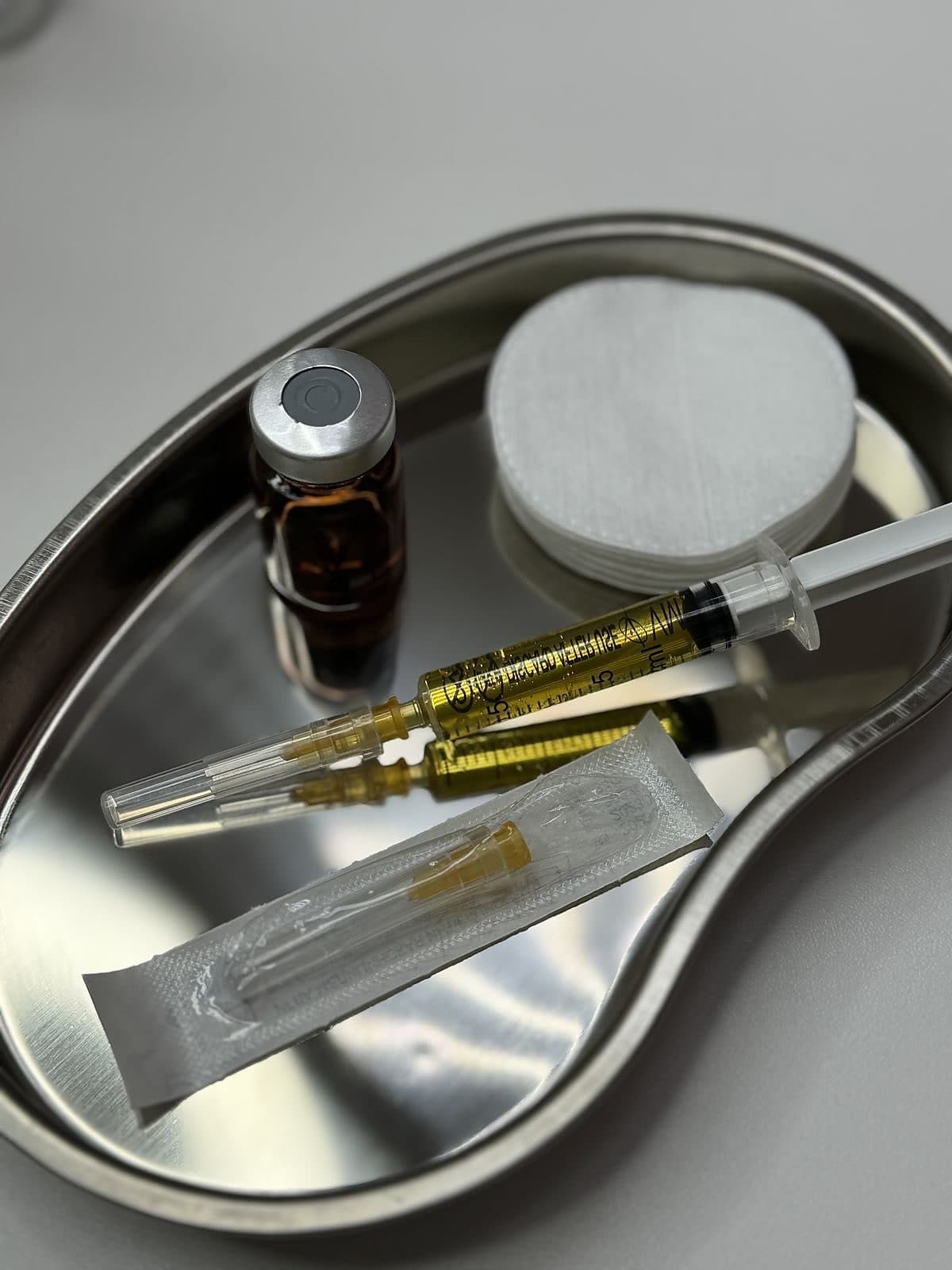 A vial, syringe and cotton laid out on a steel tray